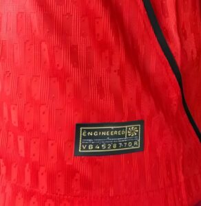 Close-up of red textured fabric with a small black label reading 'ENGINEERED' and a serial code.