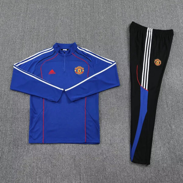 Manchester United blue training top with white stripes and crest, paired with black track pants featuring white stripes.