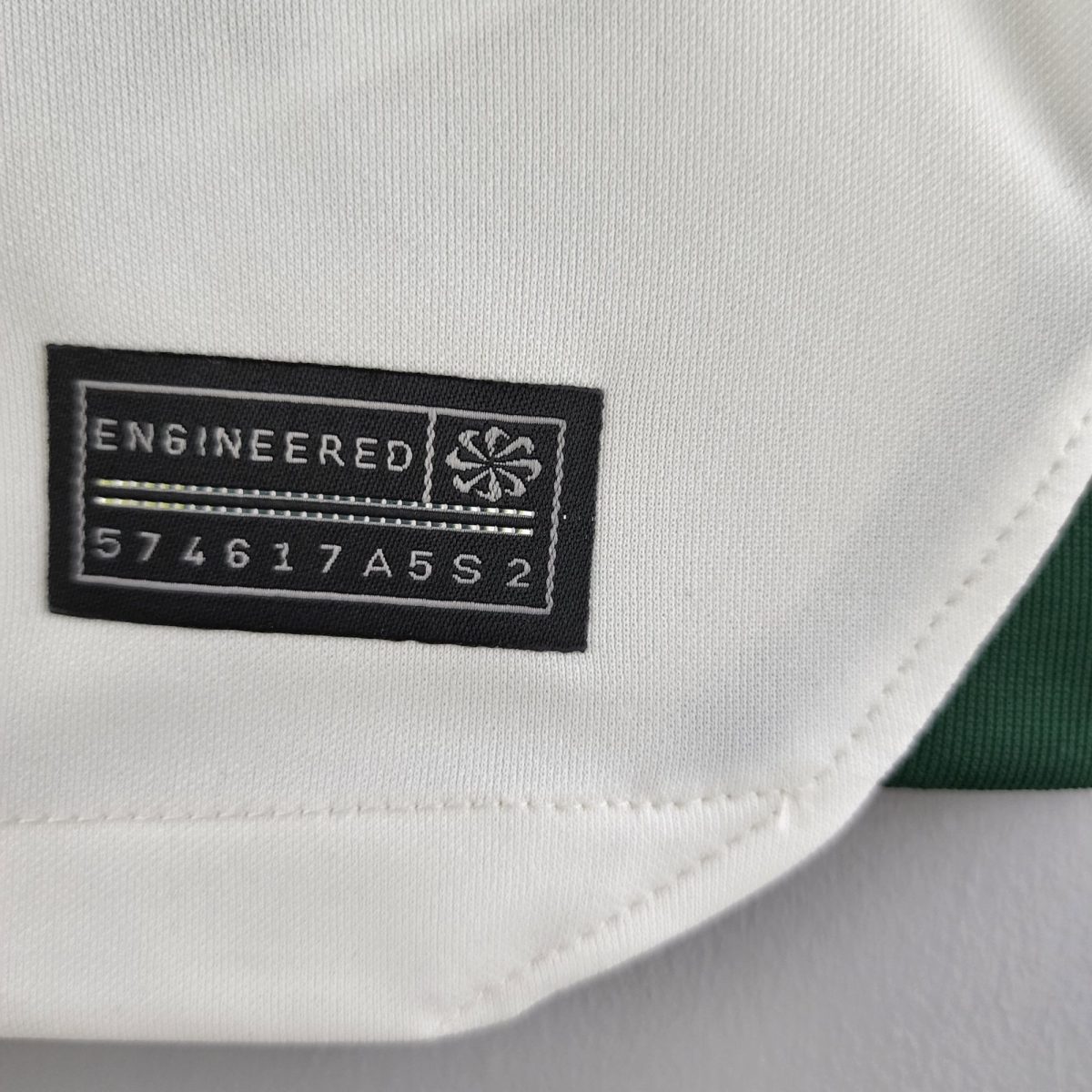 Close-up of a black sewn brand patch on white fabric, partially reading 'ENGINEERED' with a small emblem next to it.