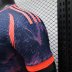 0b616aab | UAE SPORT STORE Close-up of a purple athletic jersey shoulder with bright orange stripes, wearing against a chain-link fence background.