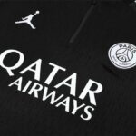 Close-up of a black Paris Saint‑Germain jersey featuring the white Qatar Airways logo and the club crest.