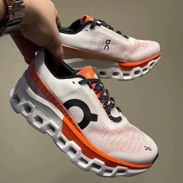 White On running shoes with orange accents and black-and-white laces being held mid-air against a neutral background, showcasing the design.