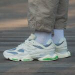 Close-up of white and blue athletic sneakers with green sole accents, paired with light blue socks and khaki pants.