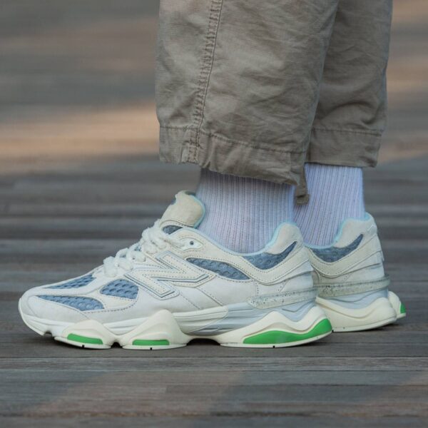 Close-up of white and blue athletic sneakers with green sole accents, paired with light blue socks and khaki pants.