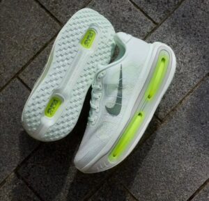 0bd453ff-3814-4640-b086-82f9cb098340 | UAE SPORT STORE White Nike running shoes with lime-green air cushioning along the sole, resting on a gray pavement surface.