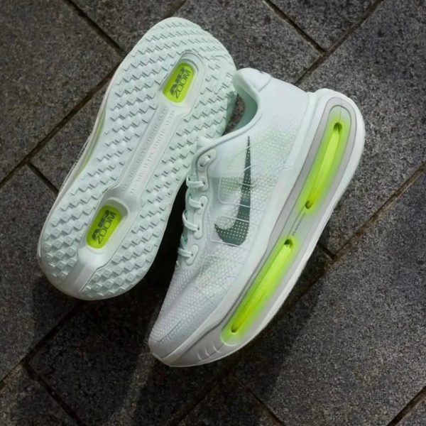 White Nike running shoes with lime-green air cushioning along the sole, resting on a gray pavement surface.