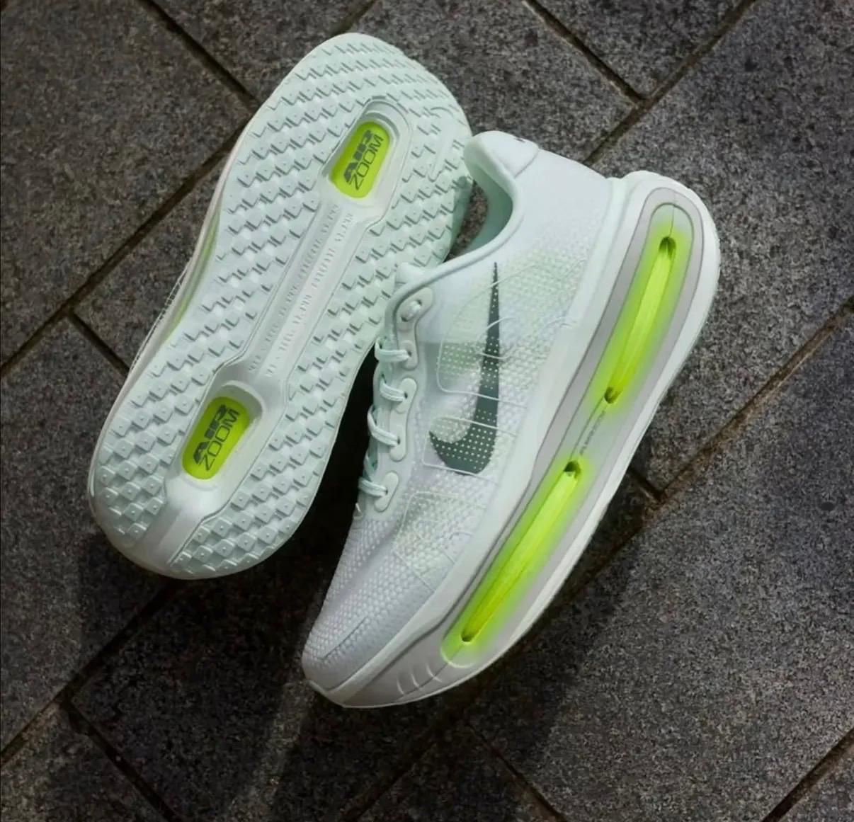 0bd453ff-3814-4640-b086-82f9cb098340 | UAE SPORT STORE White Nike running shoes with lime-green air cushioning along the sole, resting on a gray pavement surface.