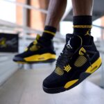 Close-up of black and yellow Air Jordan sneakers being worn, captured mid-step on a ledge or walkway.