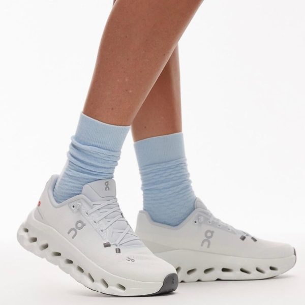 Close-up of white On running shoes and light blue socks on a person’s feet in a mid-stride pose.