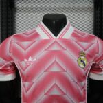 0c4e7ce8-5dab-430e-93b8-79adf43981e7 | UAE SPORT STORE Front view of a pink Real Madrid football jersey with the club crest and Adidas logo on a geometric pattern.