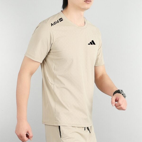 Beige Adidas athletic shirt with the logo on the chest and a small label near the left shoulder, shown from the side.