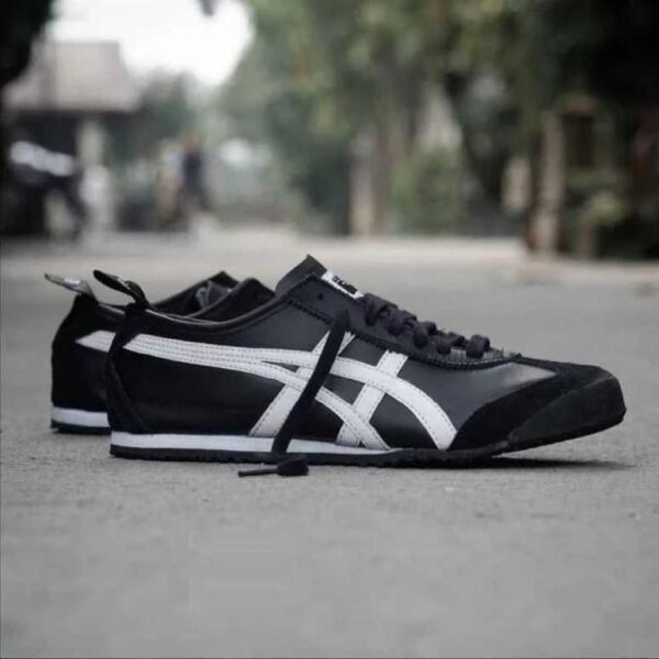 Pair of black sneakers with white stripes lying on a street surface, one shoe slightly ahead of the other on the ground.