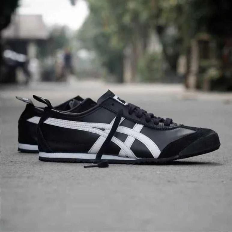 0cae50d7-d8f6-4198-a5b8-c18c4bec2316_1_b817221d-889e-472e-9087-97873e1ca3ca Pair of black sneakers with white stripes lying on a street surface, one shoe slightly ahead of the other on the ground.