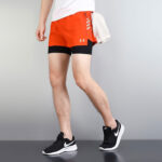 0cb86f6f | UAE SPORT STORE Person wearing bright orange athletic shorts over black compression shorts, black Nike sneakers, and a towel over the hip, standing in a stride pose.