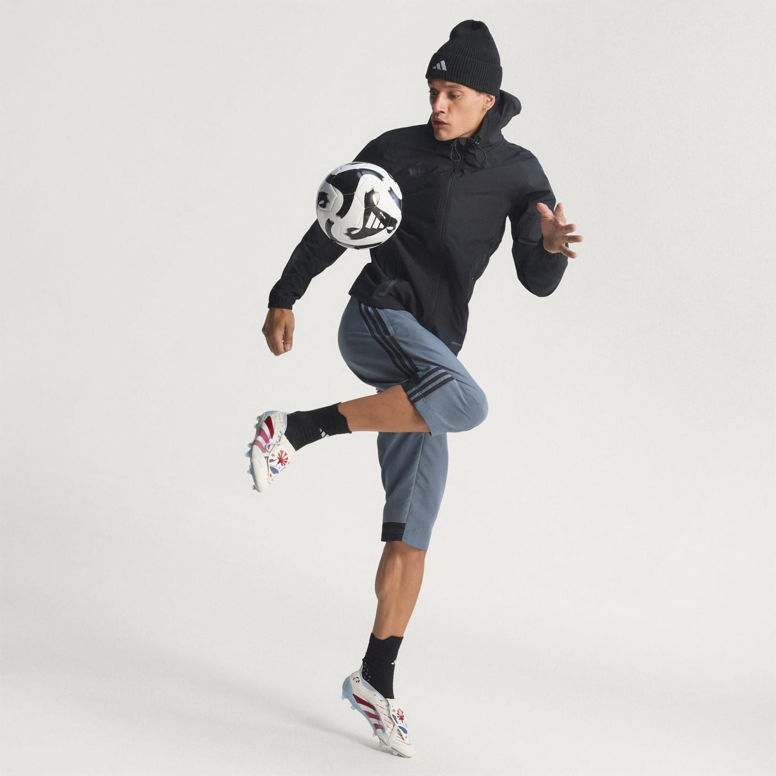 0cc8e89b-5247-4cb3-9651-ce2c8cbc0c02 | UAE SPORT STORE Athlete in a black jacket and beanie kicking a soccer ball midair