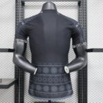 Back view of a dark athletic shirt on a mannequin in a metal rack, showcasing patterned sleeves and hem in a gym display.