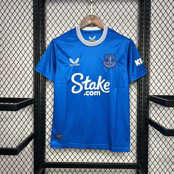 Blue Everton football jersey on a wooden hanger in a display rack, featuring sponsor Stake.com on the front and team crest on chest.