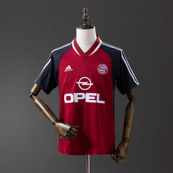 Red Bayern Munich football jersey on a mannequin, featuring navy sleeves, Adidas logo, Bayern crest, and Opel sponsor text.