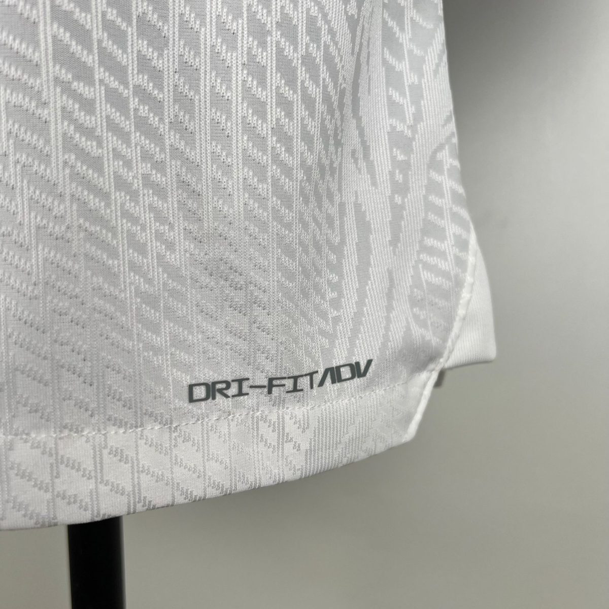 Close-up of white patterned chair fabric with the text DRI-FIT/ADV and part of a black chair leg visible to the left.