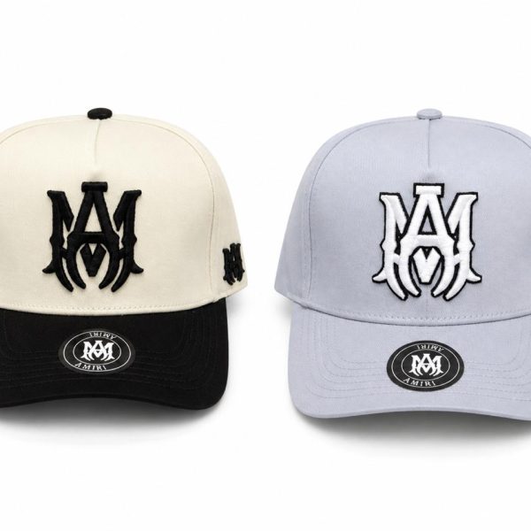 Two baseball caps displayed side by side: a beige crown with a black brim on the left and a light blue crown with a matching brim on the right, each with a bold M logo on the front and an M on the side panel.