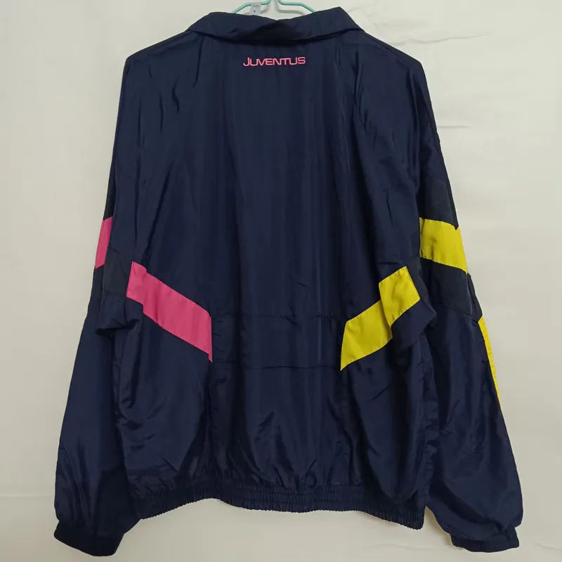 0d7e6ea077f18365 | UAE SPORT STORE Back view of a navy windbreaker with pink diagonal stripe on the left and yellow diagonal stripe on the right sleeves, Juventus logo in pink on the collar area.