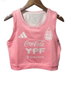 0d8e0705-284a-4b02-a249-315ed8f18f2c | UAE SPORT STORE Pink cropped athletic top with Adidas logo, Argentina crest, and sponsor logos (Coca-Cola, YPF, Binance) on chest, hanging on a wooden hanger in front of a white background.