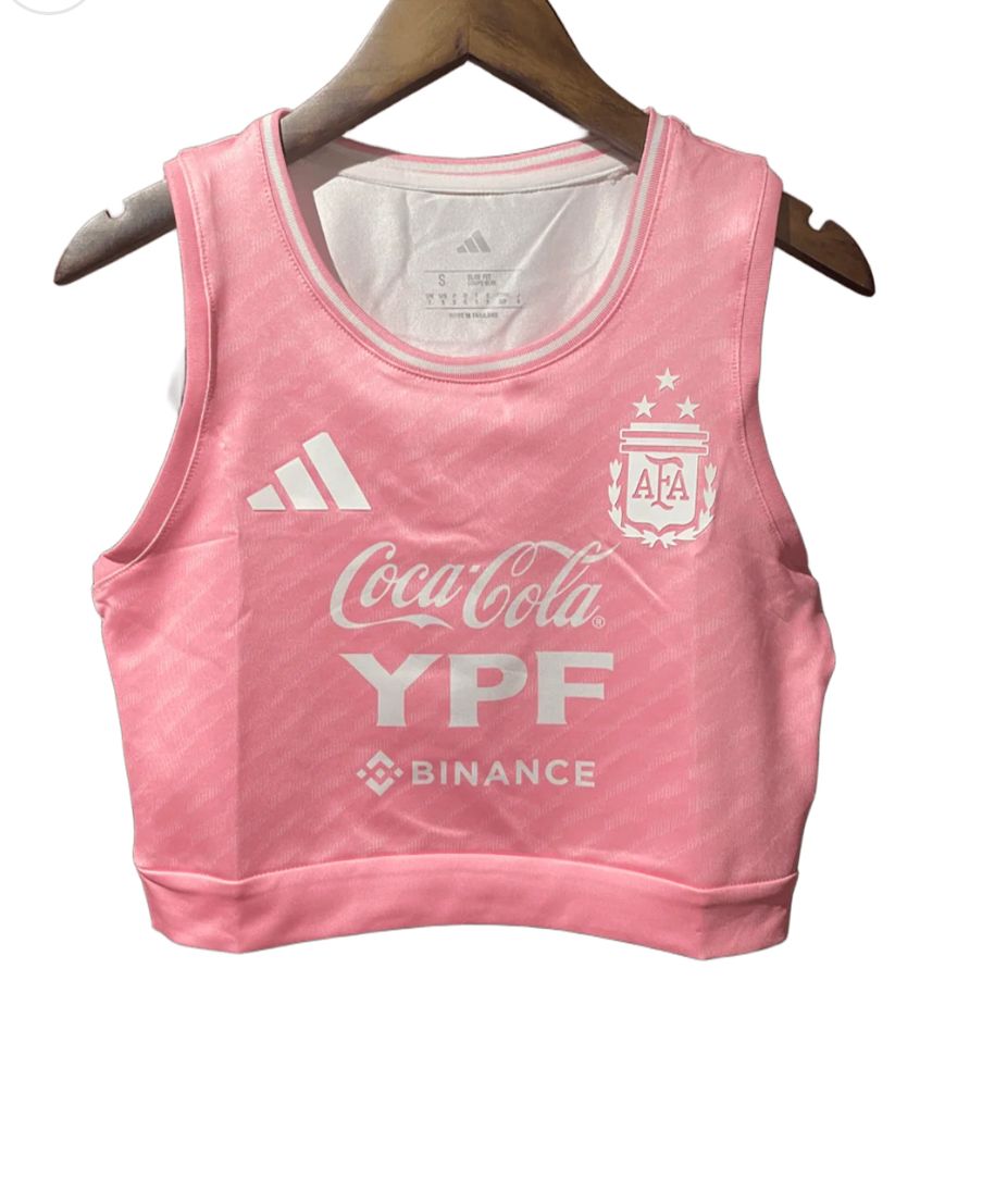 0d8e0705-284a-4b02-a249-315ed8f18f2c | UAE SPORT STORE Pink cropped athletic top with Adidas logo, Argentina crest, and sponsor logos (Coca-Cola, YPF, Binance) on chest, hanging on a wooden hanger in front of a white background.