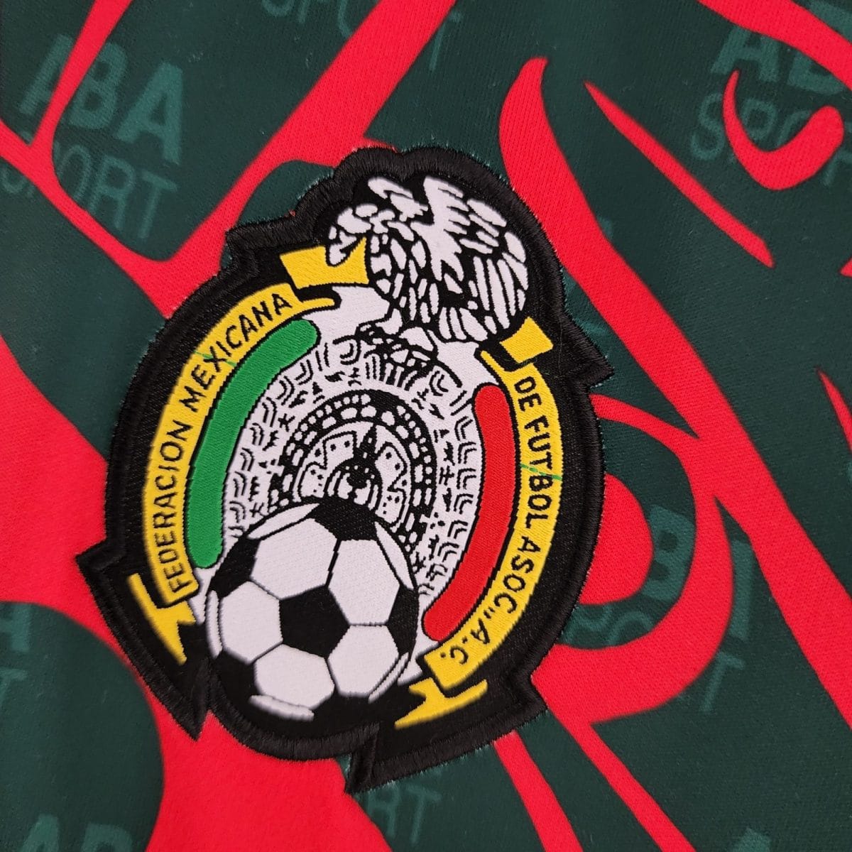 Close-up of an embroidered patch with the Mexican coat of arms (eagle and snake) in a circular border on green fabric with red accents.
