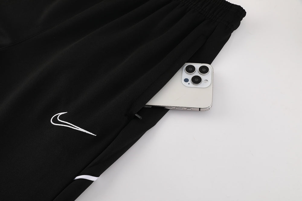 0e90c853 | UAE SPORT STORE Black Nike athletic pants with a white swoosh logo and a smartphone peeking out of the pocket nearby the leg seam, on a light background.