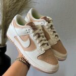 Beige and white Nike sneakers being held up, showing a perforated toe box and white laces.