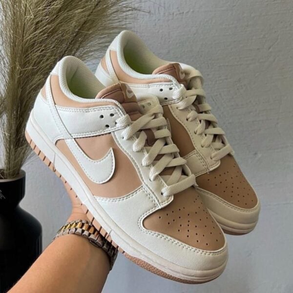 Beige and white Nike sneakers being held up, showing a perforated toe box and white laces.