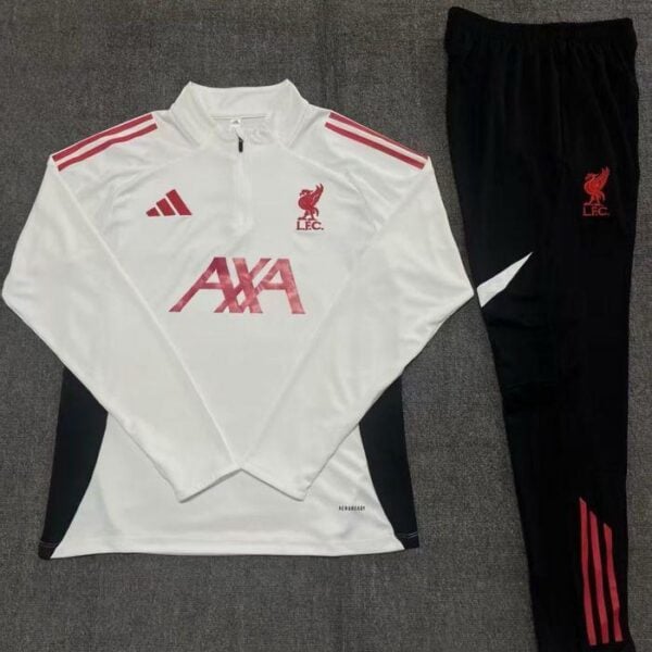 White Liverpool FC training top with red sponsor logo, red crest, and red accents paired with black pants featuring the LFC crest and stripes on a gray carpet.