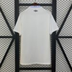 White sports jersey hanging on a hanger against a black metal lattice background; collar shows a Santos FC tag and an Umbro logo on the back of the neck area.