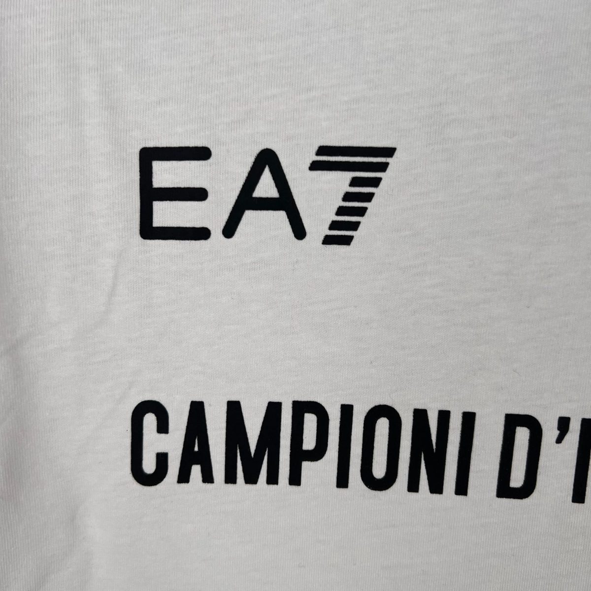 Partial view of the word 'CAMBRIDGE' printed in bold black letters on white fabric (shirt)