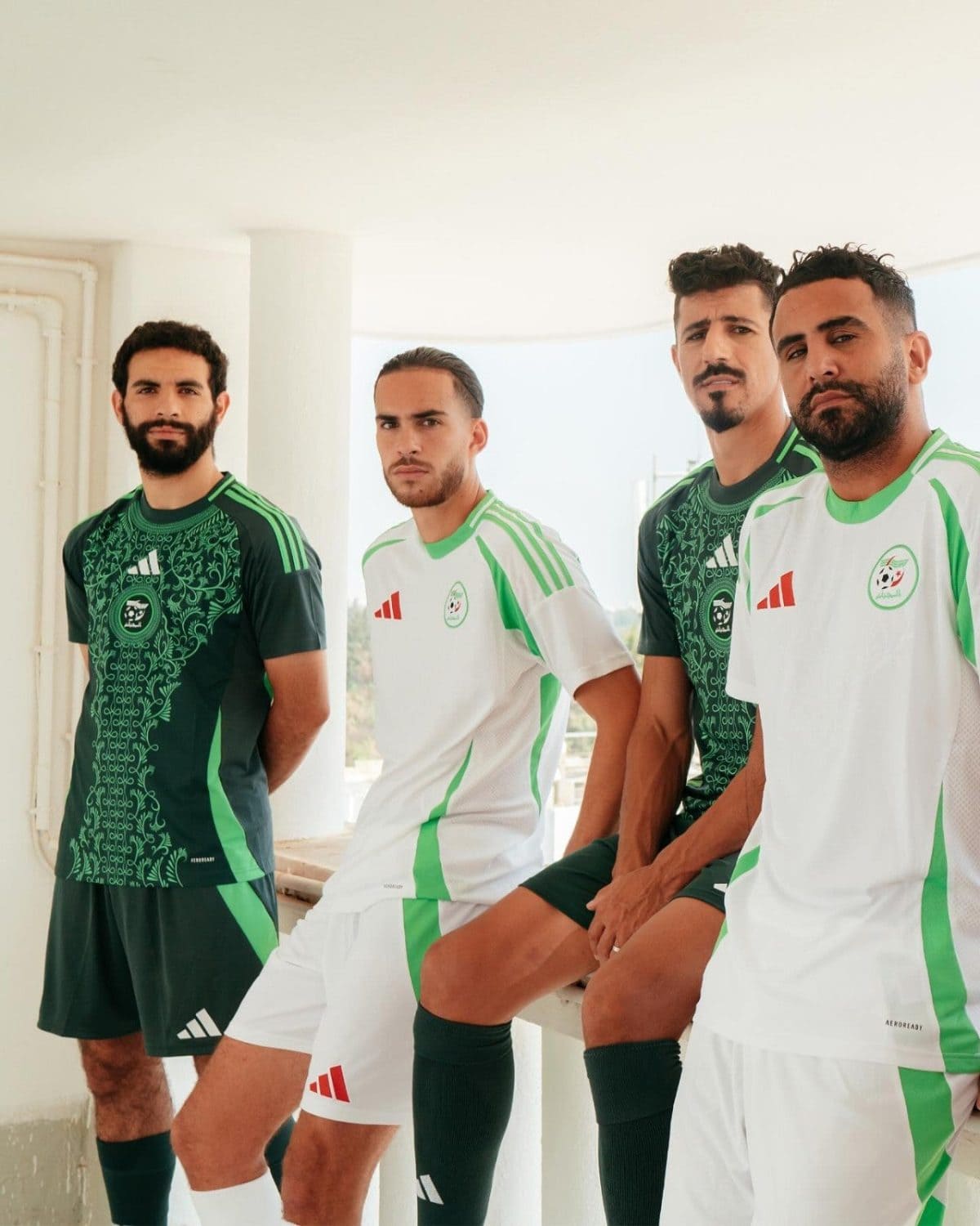 Four male soccer players in green and white uniforms pose together on a bright balcony, looking at the camera.