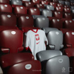 White Poland national soccer jersey draped over red stadium seats in an empty arena with eagle crest and red trim