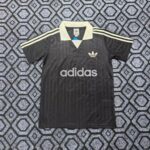 Black Adidas polo with white collar and three white stripes on sleeves, large Adidas logo and text on front resting on a patterned carpet.