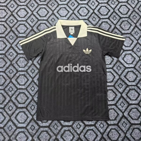 Black Adidas polo with white collar and three white stripes on sleeves, large Adidas logo and text on front resting on a patterned carpet.