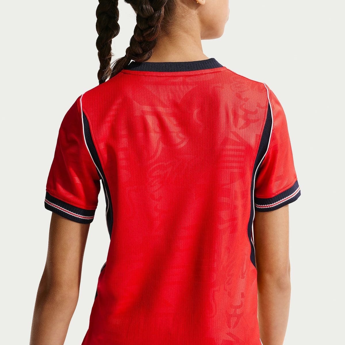 Back view of a person wearing a red athletic jersey with navy trim and braided hair visible on the left side.