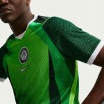 Close-up of a person wearing a bright green dotted sports jersey, with a circular federation badge on the chest and a hoop earring visible on the ear.