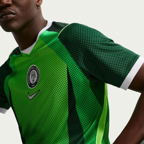 Close-up of a person wearing a bright green dotted sports jersey, with a circular federation badge on the chest and a hoop earring visible on the ear.
