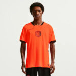 1053643_main | UAE SPORT STORE Male model wearing bright orange soccer jersey with black trim and crest, facing camera.