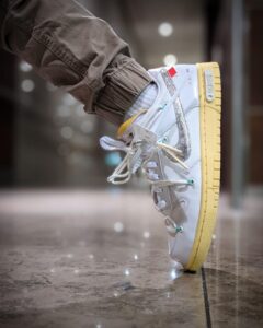 White high-top sneaker with a yellow sole is lifted mid-step on a polished floor.