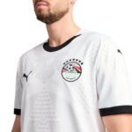 Close-up of a man wearing a white Egypt FA football jersey with a black collar and crest on the chest.