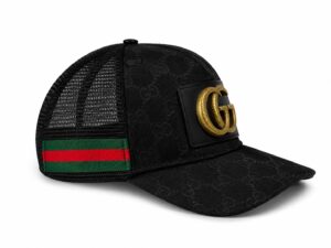 Black Gucci trucker cap with a gold double-G emblem on a leather patch and a green-red web strap at the back.
