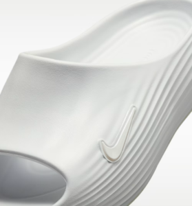 Close-up of a white Nike slide sandal, showing the embossed logo on the ribbed strap.