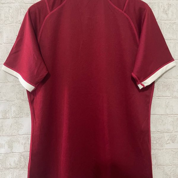 Back view of a burgundy polo shirt with a white collar and cuffs on a wooden hanger against a light brick wall.
