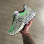 1179fdf3-12cb-4599-9352-78f3fb31e178_f6e39a38-7d95-47ba-9eb7-d98f793df827 | UAE SPORT STORE Gray-green New Balance sneaker held in a tattooed hand, showing side logo and green accents.