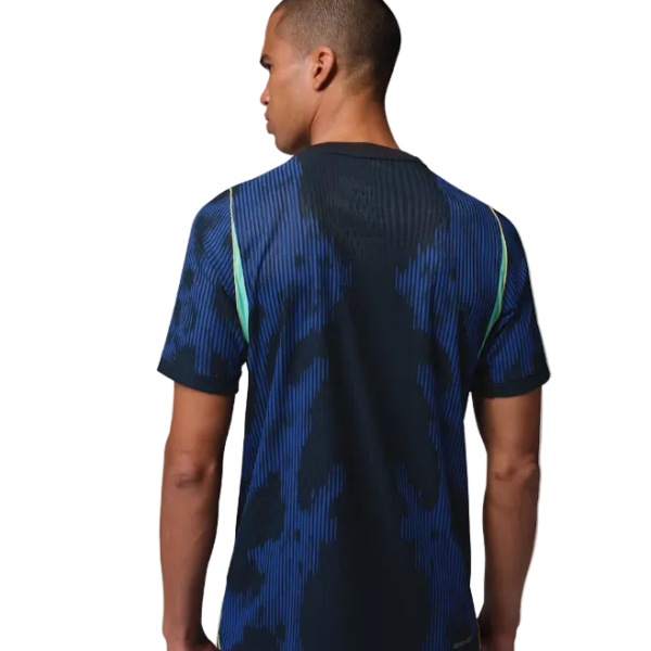 Back view of a man wearing a blue patterned short-sleeve sports jersey with dark center panel, against a white background