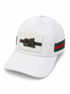White Gucci baseball cap with allover embossed GG pattern, red-green stripe, and a white patch featuring a metallic bee and 'Gucci' text